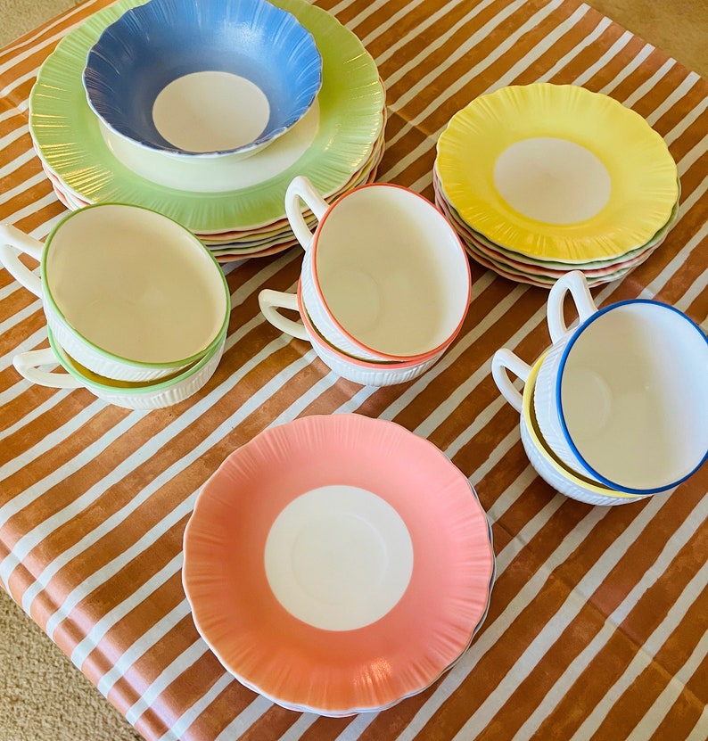May include: A set of vintage teacups and saucers in various pastel colors, including pink, yellow, blue, and green. The cups and saucers have a scalloped edge and a delicate floral design.