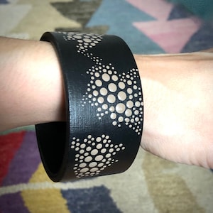 May include: A black bracelet with a repeating pattern of beige circles in a geometric design.