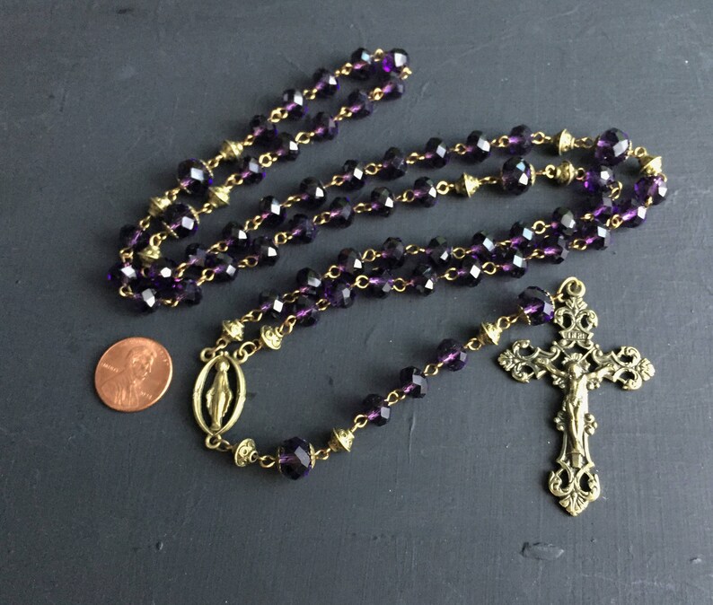 Puede incluir: Un rosario de cristal morado con detalles dorados y un crucifijo dorado con una figura de Jesucristo.
