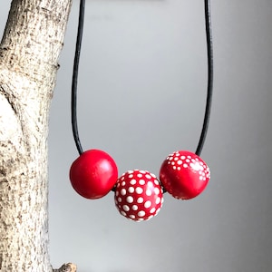 Op de afbeelding: Een rode en witte stippenketting met drie grote ronde kralen. De ketting is gemaakt met een zwart koord.