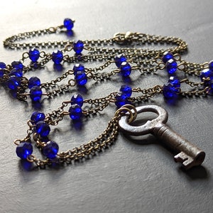 May include: A necklace with a large antique key pendant and blue glass beads on a brass chain.