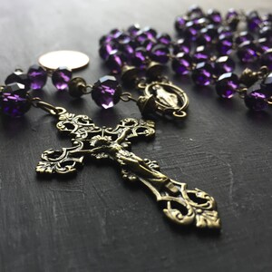Puede incluir: Un rosario de cristal morado con un crucifijo de lat&oacute;n y un dije de lat&oacute;n de la Virgen Mar&iacute;a. Las cuentas del rosario son facetadas y tienen un color morado oscuro.