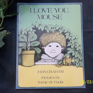 May include: A children's book cover with a green background. The title is "I Love You, Mouse" in white text. The author is John Graham and the illustrator is Tomie de Paola. The cover features a boy with brown hair looking out a window with a mouse peeking out from behind a plant.