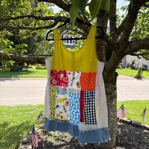 May include: A sleeveless tank top featuring a mustard yellow upper section and a patchwork lower body. The patchwork includes various Dr. Seuss character prints, red floral patterns, orange geometric shapes, blue floral fabric, and a denim hem.