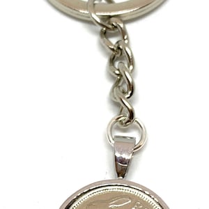 Puede incluir: Un llavero plateado con un dije redondo en forma de moneda que presenta una liebre plateada en un lado y el texto "Eire" y "3p" en el otro.