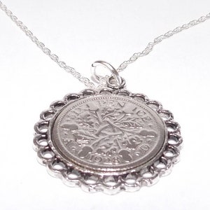 May include: A silver necklace featuring a vintage coin pendant. The coin is set in a decorative, scalloped silver frame and hangs from a delicate chain. The coin's details are visible, showcasing its design.