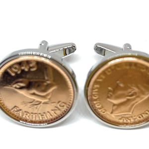May include: A pair of cufflinks featuring a 1943 British Farthing coin. The cufflinks are silver-toned with a copper-colored coin insert.