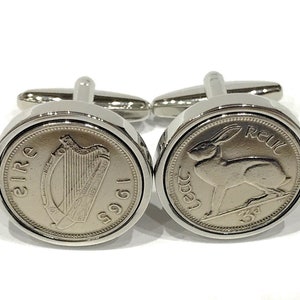 May include: A pair of silver cufflinks featuring Irish coins. One cufflink has a harp design with the text "EIRE 1961", and the other cufflink has a hare design with the text "3d REIL".