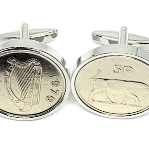 Puede incluir: Un par de gemelos de plata con una moneda irlandesa de 5 peniques de 1970 con un arpa en un lado y un toro en el otro.