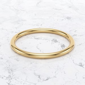 Könnte beinhalten: Ein einfacher, goldfarbener Ring mit glatter, polierter Oberfläche. Der Ring ist kreisförmig und scheint aus Metall zu sein. Der Ring ist vor einem weißen und grauen Marmorhintergrund platziert. Der Ring ist ein Schmuckstück.