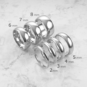 Op de afbeelding: Een collectie van zeven gepolijste zilverkleurige metalen ringen gerangschikt in een groep. Elke ring is gelabeld met de specifieke breedte, variërend van 2 mm tot 8 mm, wat de beschikbare maatopties voor deze gladde, ronde ringen duidelijk aangeeft.