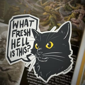 Könnte beinhalten: Ein schwarzer Katzenaufkleber mit gelben Augen und weißen Schnurrhaaren. Der Aufkleber hat den Text "WHAT FRESH HELL IS THIS?" in einer weißen Sprechblase. Der Künstlername ArtistAbe steht unten.