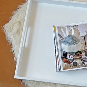 May include: A square white serving tray with cutout handles containing a stack of magazines. The top magazine is an Architectural Digest issue featuring a living room interior and the text At Home With Julianne Moore.