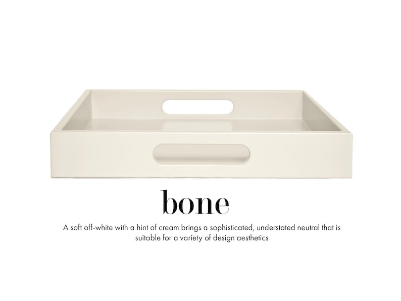 May include: A rectangular off-white tray with a smooth finish and two integrated oval handles on the sides. The text "bone" is printed below the tray, followed by the description: "A soft off-white with a hint of cream brings a sophisticated, understated neutral that is suitable for a variety of design aesthetics."