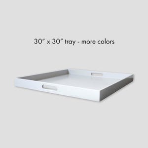 May include: A square white tray with integrated cutout handles on two sides. The tray features a smooth, glossy finish and is labeled with the text 30" x 30" tray - more colors. The design is simple, featuring raised edges and a flat base.