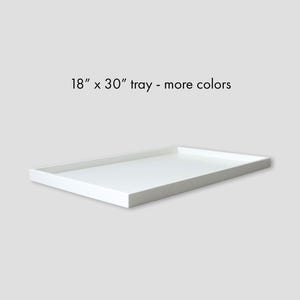 May include: A rectangular white tray, measuring 18 x 30 inches, is displayed against a light gray background. The tray has a simple, clean design with a slightly raised edge. Text on the image reads: "18" x 30" tray - more colors."