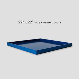 May include: A square blue tray with raised edges, featuring the text 22" x 22" tray - more colors printed above it. The tray has a smooth, solid-colored surface and a low-profile design, presented from a slightly elevated angle.