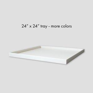 May include: A square white tray with raised edges, featuring the text 24" x 24" tray - more colors printed above it. The tray has a smooth, flat surface and a clean, simple design, presented against a plain, light gray background.