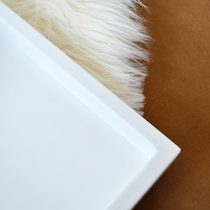 May include: A rectangular white tray with a smooth, solid surface and raised edges. The tray features a clean, minimalist design with a flat base and a uniform white finish, providing a simple and functional structure for various organizational needs.