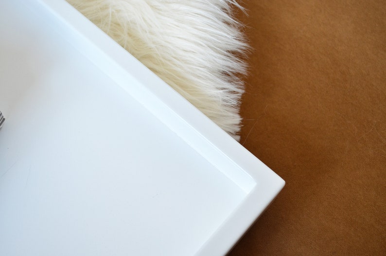 May include: A rectangular white tray with a smooth, solid surface and raised edges. The tray features a clean, minimalist design with a flat base and a uniform white finish, providing a simple and functional structure for various organizational needs.