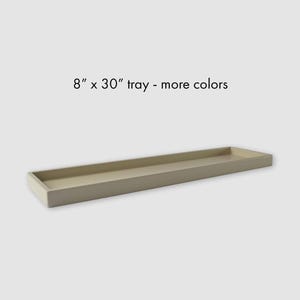 May include: A long, rectangular, beige-colored tray with low, straight sides. The text "8" x 30" tray - more colors" is printed in black above the tray, indicating its dimensions in inches and that other color options are available.