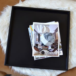 May include: A square black tray with a raised rim holding a stack of magazines. The top magazine features the Architectural Digest logo, a large white geometric shape, and the text At Home With Julianne Moore, The Movie Star Next Door.