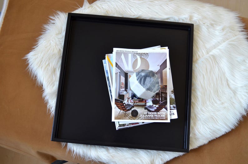 May include: A square black tray with a raised rim holding a stack of magazines. The top magazine features the Architectural Digest logo, a large white geometric shape, and the text At Home With Julianne Moore, The Movie Star Next Door.
