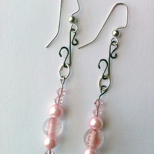 May include: A pair of silver dangle earrings with pink and clear glass beads. The earrings feature a delicate, twisted design.