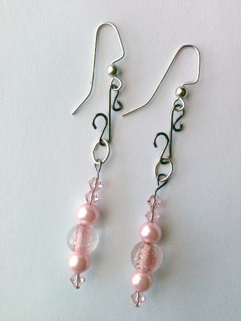 May include: A pair of silver dangle earrings with pink and clear glass beads. The earrings feature a delicate, twisted design.