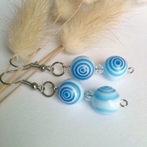 May include: A pair of blue and white striped earrings with silver hooks. The earrings are made of glass beads with a swirling pattern.