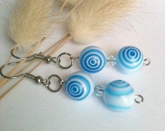 May include: A pair of blue and white striped earrings with silver hooks. The earrings are made of glass beads with a swirling pattern.