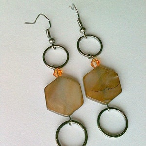 May include: A pair of silver earrings with a hexagonal shell-like pendant and a small orange crystal bead. The earrings have a silver hoop and a silver hook.