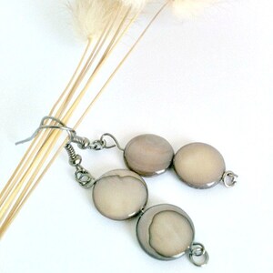 May include: A pair of silver tone earrings with three round, cream-colored, iridescent shell beads.