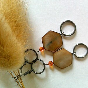 May include: A pair of earrings with hexagonal brown and white shell-like pendants and orange crystal accents. The earrings are attached to silver hoops.