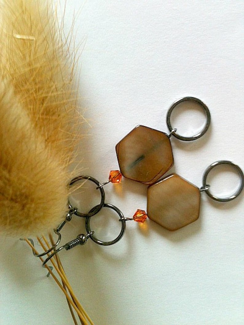 May include: A pair of earrings with hexagonal brown and white shell-like pendants and orange crystal accents. The earrings are attached to silver hoops.