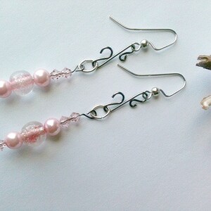 May include: A pair of dangle earrings with pink beads and clear glass beads. The earrings have silver hooks and a silver chain.