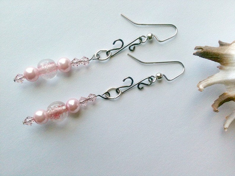 May include: A pair of dangle earrings with pink beads and clear glass beads. The earrings have silver hooks and a silver chain.