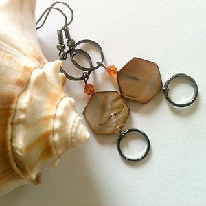 May include: A pair of earrings with a hexagonal shell pendant and a silver hoop. The earrings are hanging from a seashell.