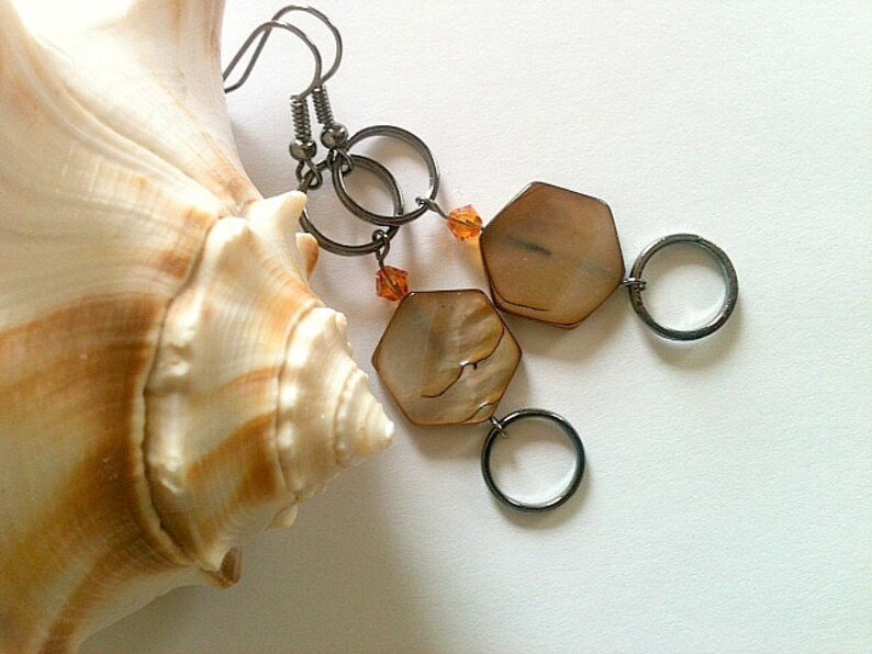 May include: A pair of earrings with a hexagonal shell pendant and a silver hoop. The earrings are hanging from a seashell.