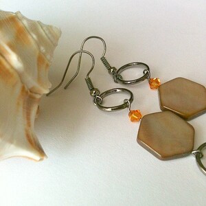 May include: A pair of earrings with a hexagonal shaped pendant made of brown mother of pearl. The earrings have a silver hook and a small orange crystal bead.
