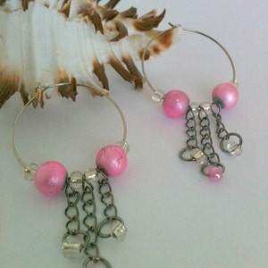 May include: Pink hoop earrings with silver chains and beads. The earrings have a dangling charm with a pink bead.