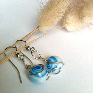 May include: A pair of silver earrings with blue and white swirl glass beads wrapped in silver wire.