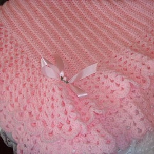 Peut inclure: Une couverture pour bébé en crochet rose avec un bord festonné et un nœud en satin rose.