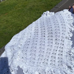 May include: White crocheted baby blanket with a delicate lace pattern and scalloped edges.