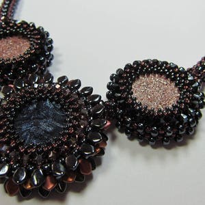 May include: A beaded necklace with three large, round pendants. The pendants are made of dark brown and black beads and have a metallic sheen. The center pendant is larger than the other two and has a dark blue center.