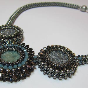 May include: A silver and blue beaded necklace with three round pendants. The pendants are made of silver beads and have a center piece of blue.