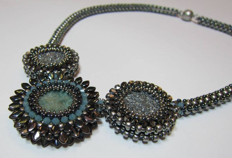 May include: A silver and blue beaded necklace with three round pendants. The pendants are made of silver beads and have a center piece of blue.