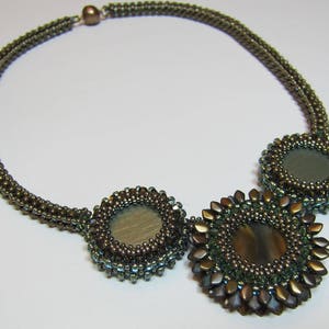 May include: A brown beaded necklace with three round, green and brown, beaded pendants. The pendants have a mirrored surface.