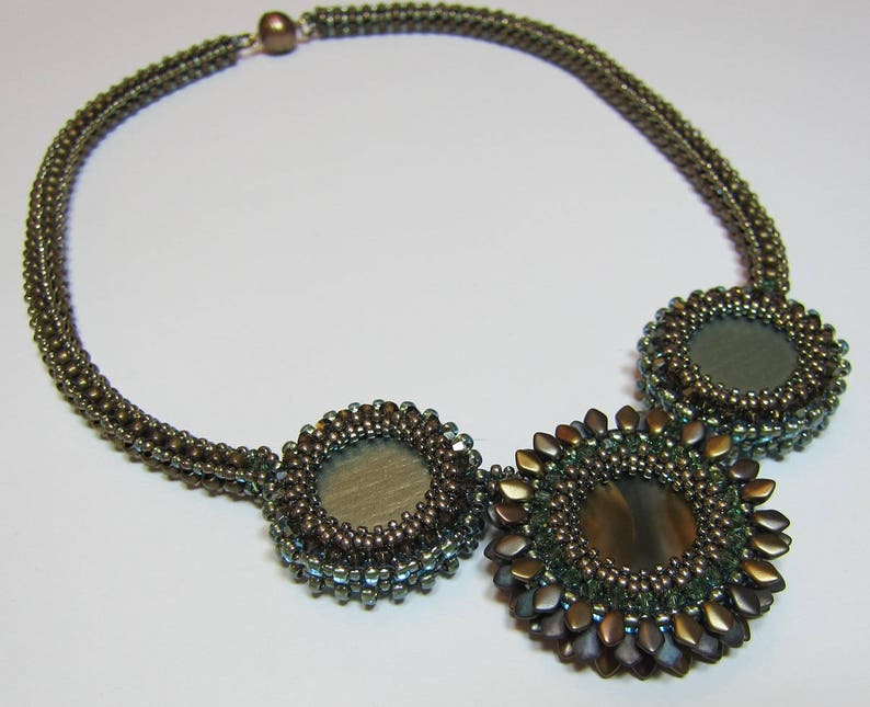 May include: A brown beaded necklace with three round, green and brown, beaded pendants. The pendants have a mirrored surface.