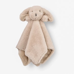 May include: A plush, beige dog-shaped security blanket. The dog has floppy ears, a small nose, and embroidered eyes. The blanket portion is a soft, square shape with a contrasting, smooth backing. A comforting item for babies and toddlers.